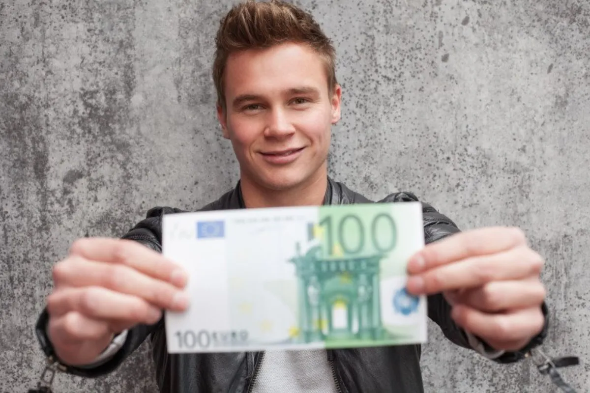 Junger Mann zeigt einen 100-Euro-Schein — Ausbildungsgehalt in der Pflege